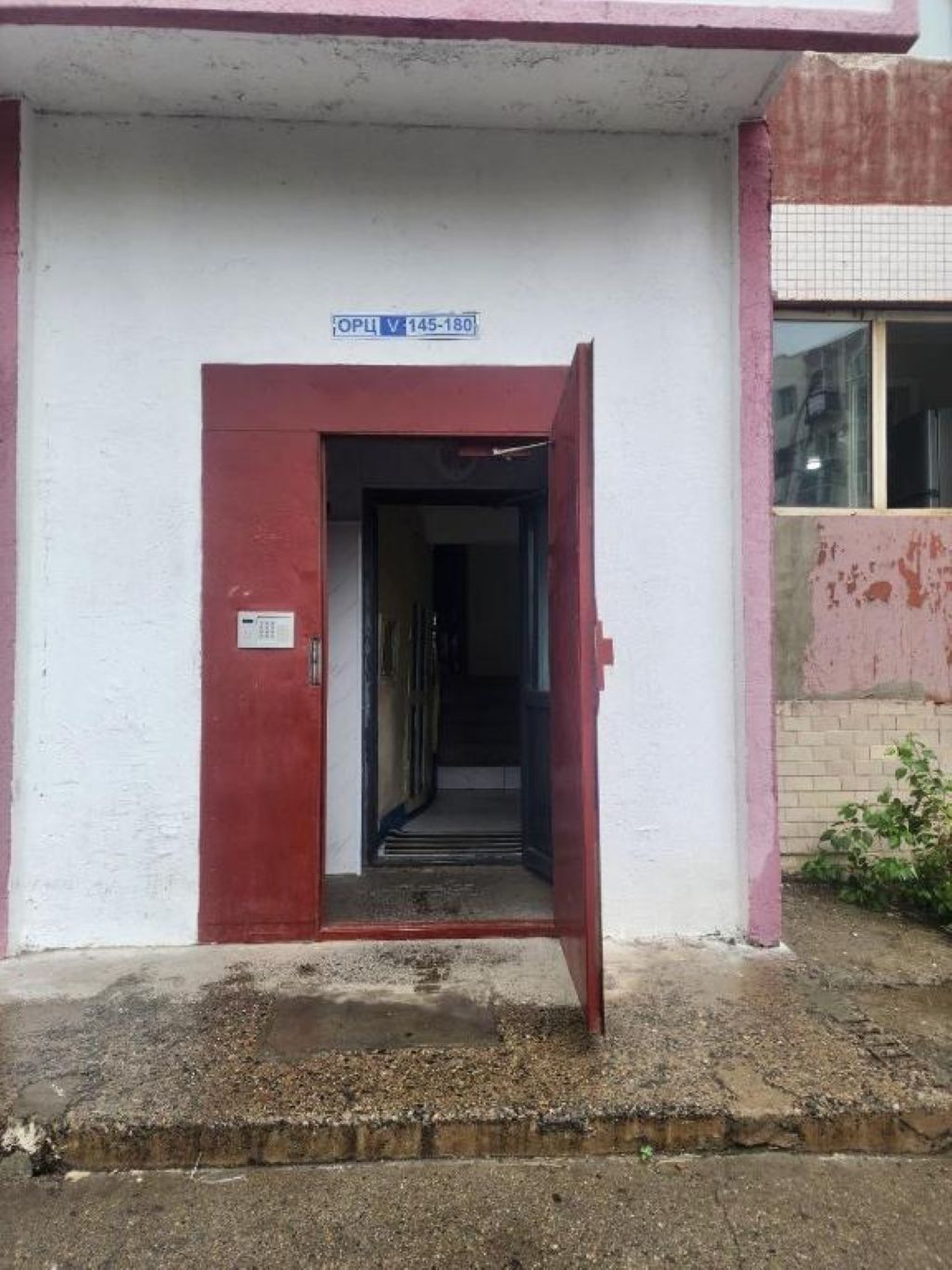 A building entrance with a red door, a visible sign above the door, and a small window to the right.
