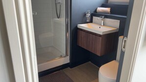 Un baño con cabina de ducha de vidrio, lavamanos con tocador de madera y un inodoro.