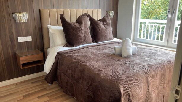 Un dormitorio con cama, almohadas, una mesita de noche y una ventana con vistas.