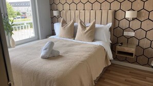 Habitación de hotel con cama, mesita de noche, lámpara y vistas al exterior.