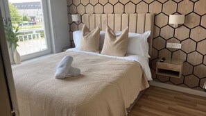 A hotel room with a bed, a bedside table, a lamp, and a view of the outside. - Spacious 5BR Townhouse with Free Parking (Glasgow)