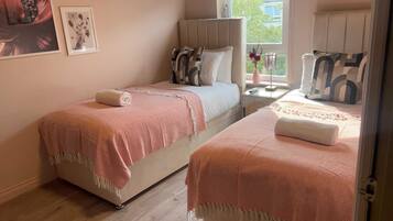 A bedroom with two beds, a bedside table with a lamp, and a window with a view.