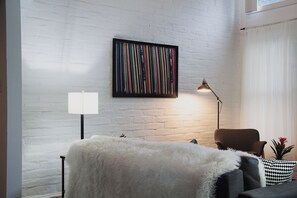 Ein modernes Wohnzimmer mit einer weißen Ziegelwand, einem gerahmten abstrakten Gemälde, einer Stehlampe, einem braunen Sessel und einem kleinen Blumentopf.