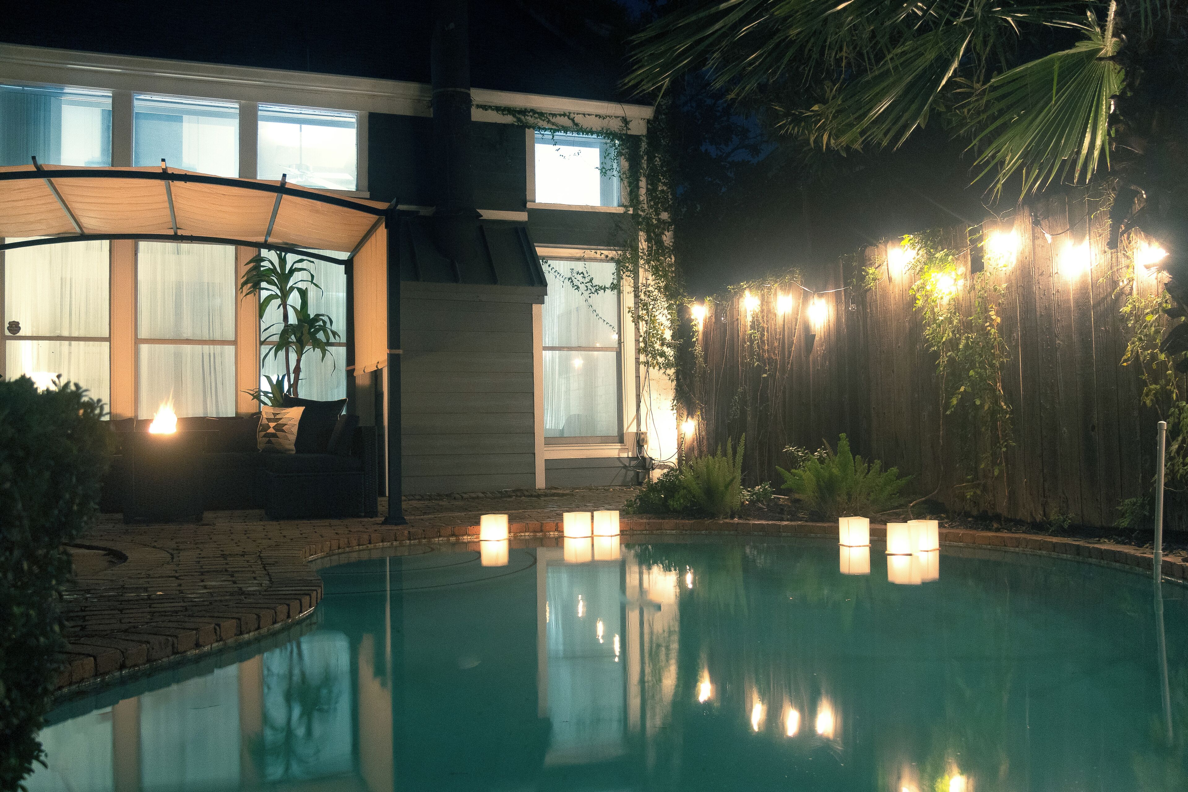A swimming pool with a covered seating area and string lights.