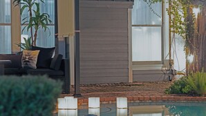 Uma área de piscina com um deck de madeira, um sofá com almofadas e um vaso de planta.