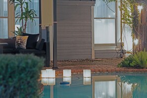 Ein Poolbereich mit Holzterrasse, einer Couch mit Kissen und einem Blumentopf.