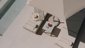 A poolside lounge area with a sunbed, a small table with a bowl of fruit and a glass of water, and a hat. - Lynx Villa, Heated Pool, Walk to Shops & Dining (Rethymno)