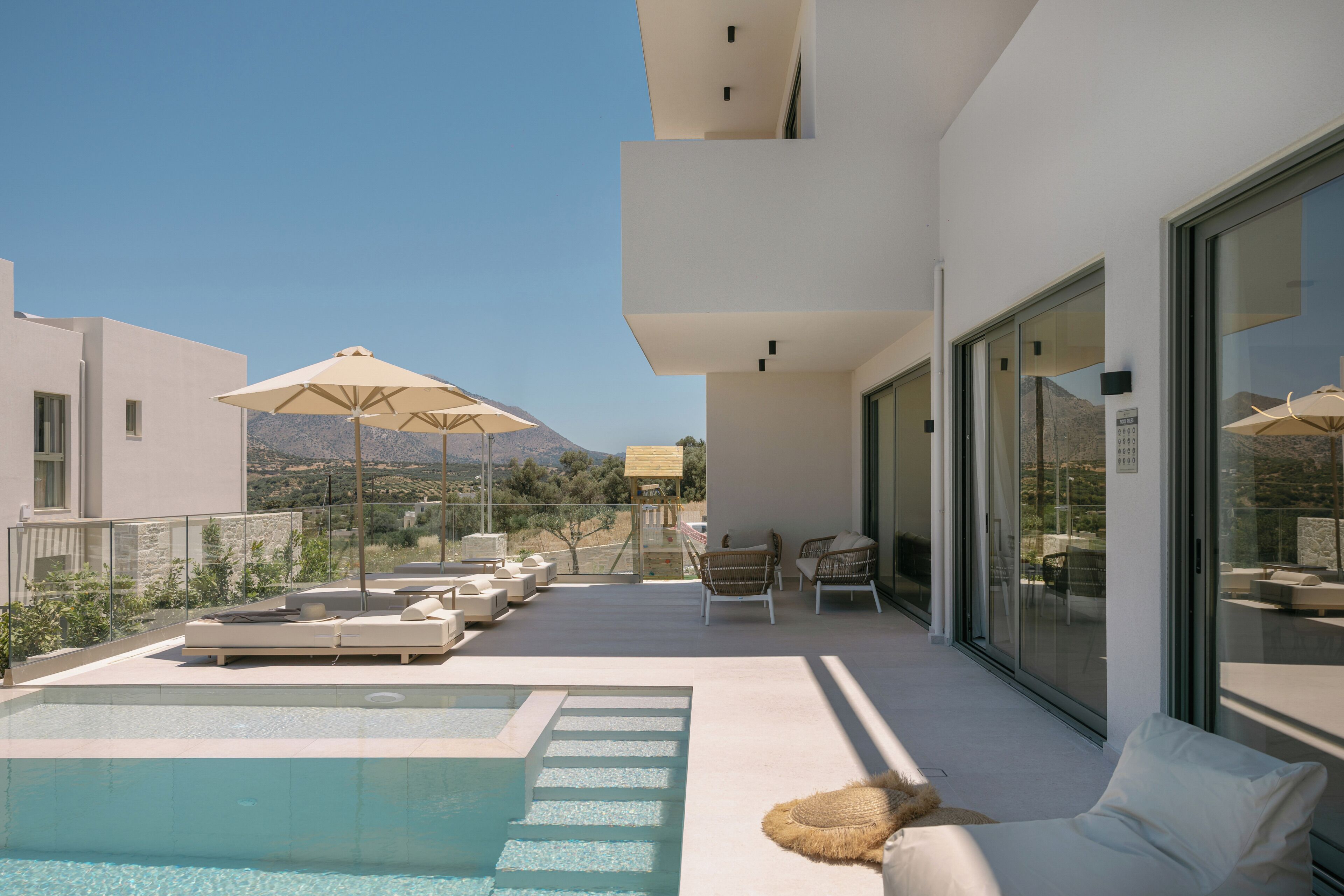 A modern outdoor pool area with lounge chairs and umbrellas, surrounded by a glass railing.