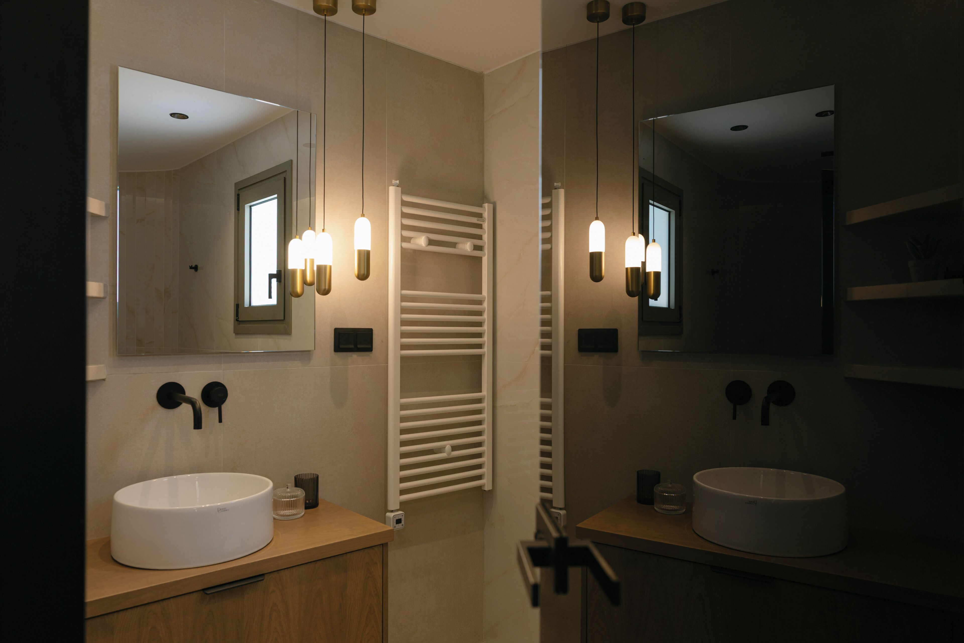 A modern bathroom with two sinks, a towel rack, and pendant lights.