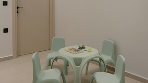 A room with a beige door, a round table with chairs, and a small play area with toys. - Lynx Villa, Heated Pool, Walk to Shops & Dining (Rethymno)