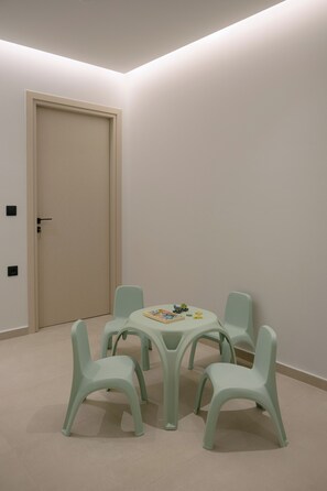 A room with a beige door, a round table with chairs, and a small play area with toys. - Lynx Villa, Heated Pool, Walk to Shops & Dining (Rethymno)