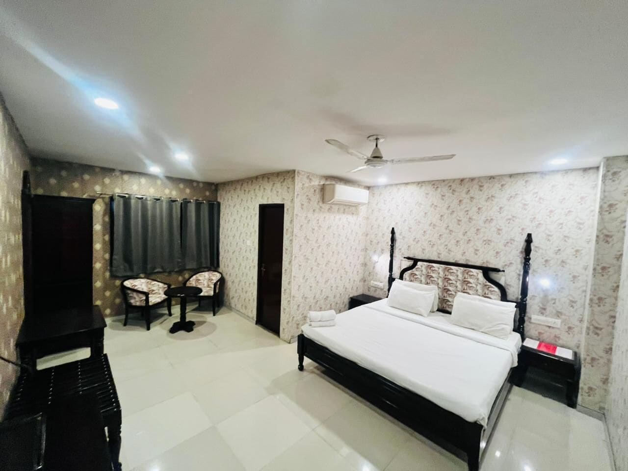 A bedroom with a bed, a ceiling fan, a TV, and a small table with chairs.