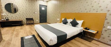 A bedroom with a bed, bedside table, nightstand, desk, chair, and a mirror on the wall.