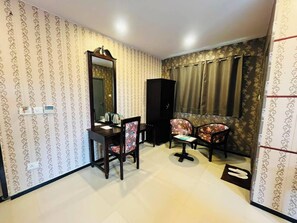 A room with patterned wallpaper, a large mirror, a desk with a chair, a cabinet, and a sofa with curtains. - Hotel Elite Stay By The Rahul (Nagpur)