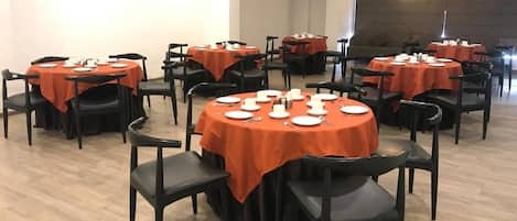 A dining area with round tables, black chairs, and orange tablecloths.