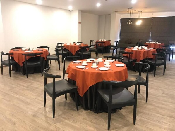 A dining area with round tables, black chairs, and orange tablecloths.