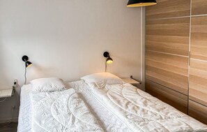 A double bed with white bedding, two wall-mounted lamps, a wooden panel wall, and a nightstand with a lamp. - 4 bedroom awesome home in Væggerløse (Væggerløse)