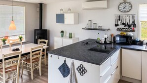 Ett modernt kök med en central köksö, vita köksskåp, en svart spis och olika köksredskap som hänger på väggen.