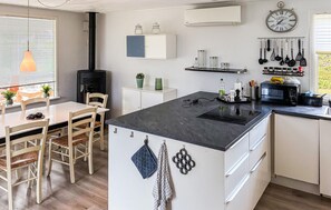 A modern kitchen with a central island, white cabinetry, a black stove, and various kitchen utensils hanging on the wall. - 4 bedroom awesome home in Væggerløse (Væggerløse)