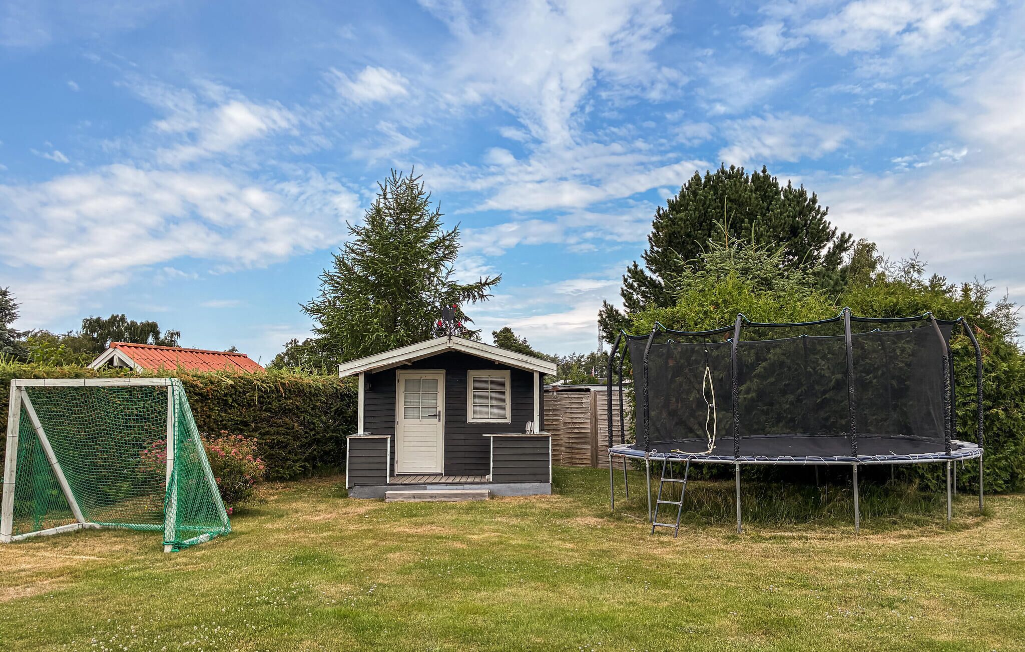 A small house with a porch, a trampoline, and a green netted play area.
