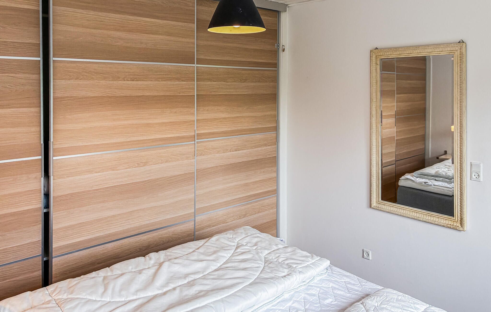 A bedroom with a bed, a wooden wardrobe, a mirror, and a pendant light.