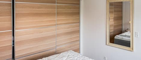 A bedroom with a bed, a wooden wardrobe, a mirror, and a pendant light.
