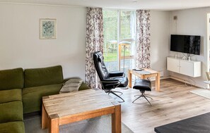 A living room with a green sofa, a wooden coffee table, a black leather chair, a small wooden side table, and a television on a white cabinet. - 4 bedroom awesome home in Væggerløse (Væggerløse)