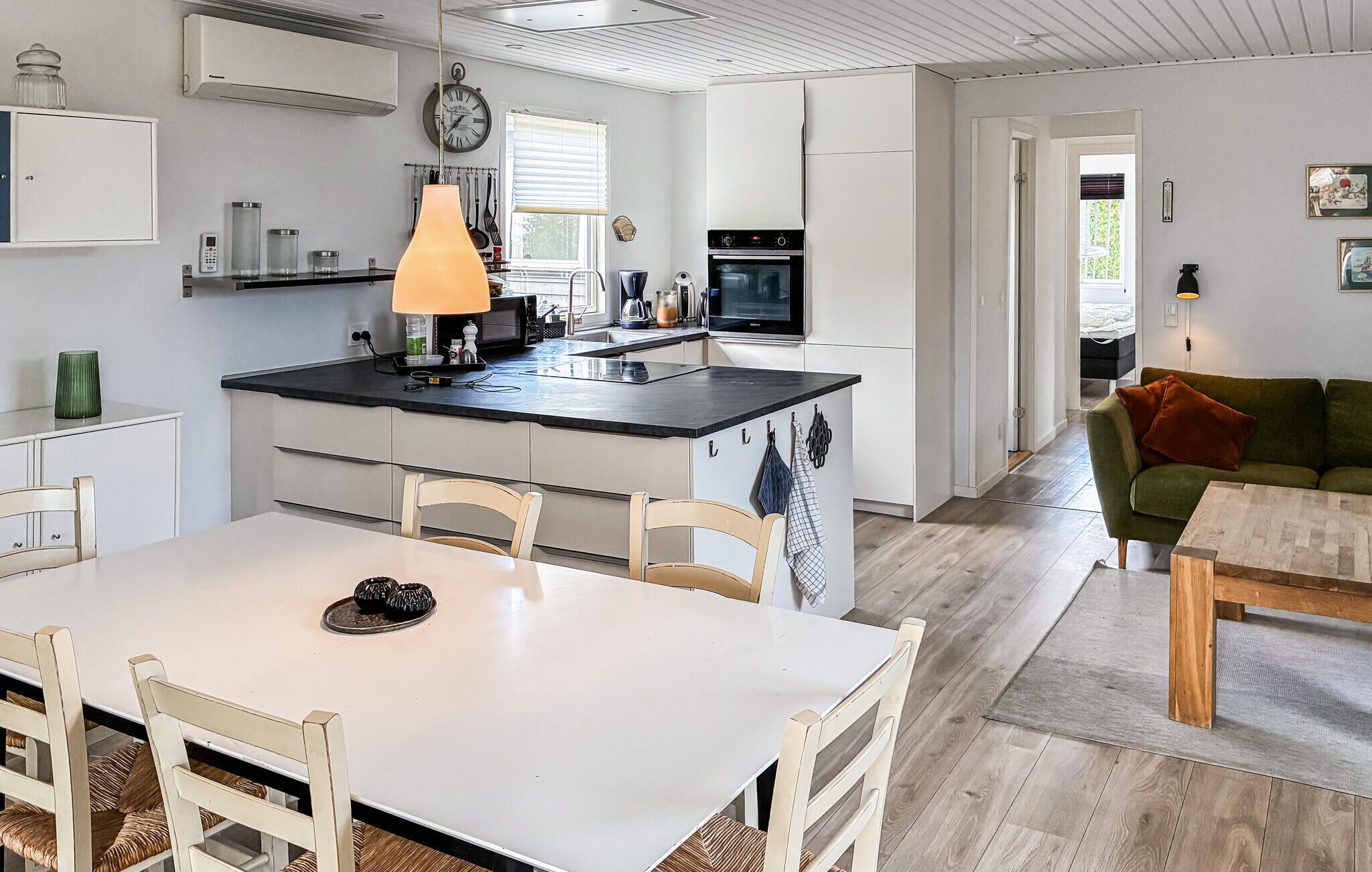 A modern kitchen with a central island, a dining area with a white table and chairs, and a living room with a green sofa and a wooden coffee table.
