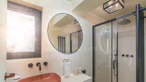 A bathroom with a round mirror, a sink, and a glass-enclosed shower. - Villa Le Sfumature Mediterranee - Sardinia Unlimited (San Teodoro)