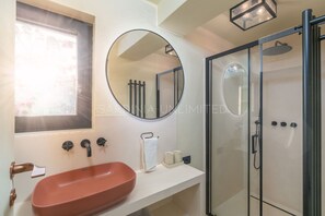 A bathroom with a round mirror, a sink, and a glass-enclosed shower. - Villa Le Sfumature Mediterranee - Sardinia Unlimited (San Teodoro)
