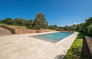 A rectangular pool with stone steps leading up to it, surrounded by a stone wall and a grassy area with trees. - Villa Le Sfumature Mediterranee - Sardinia Unlimited (San Teodoro)