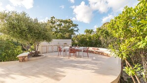 A covered outdoor patio with a table and chairs, surrounded by stone walls and greenery. - Villa Le Sfumature Mediterranee - Sardinia Unlimited (San Teodoro)
