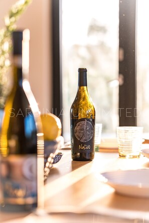 A bottle of wine on a table with a window in the background. - Villa Le Sfumature Mediterranee - Sardinia Unlimited (San Teodoro)