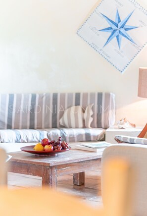Ein Zimmer mit einem Holztisch, einer Obstplatte, einer Couch mit gestreiften Kissen und einer Wand mit Kompass-Dekoration.