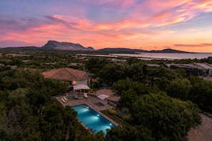 Une piscine entourée d’une végétation luxuriante, une montagne en arrière-plan et un ciel au coucher du soleil.