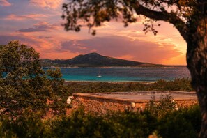 Un paysage côtier offrant une vue dégagée sur la mer, avec un voilier et une montagne à l’horizon.