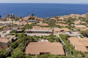An aerial view of a coastal residential area with terracotta-roofed houses, a marina, and rocky terrain. - Villetta Luce Marina - Sardinia Unlimited (Costa Paradiso)