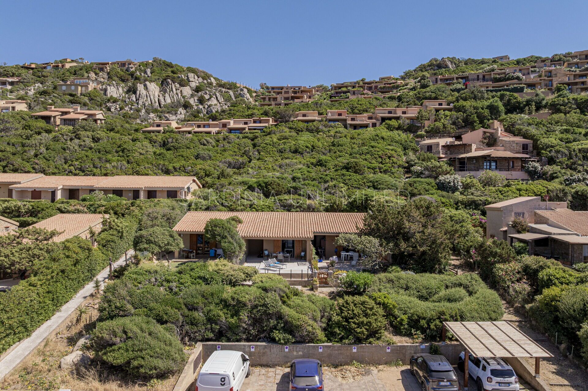 A hillside residential area with terraced houses, a parking area, and a central building with a patio.