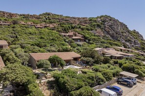 A hillside residential area with terraced houses, a swimming pool, and parked vehicles. - Villetta Luce Marina - Sardinia Unlimited (Costa Paradiso)