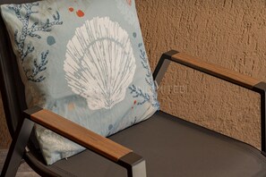 A chair with a mesh backrest and wooden armrests, positioned against a textured wall. - Villetta Luce Marina - Sardinia Unlimited (Costa Paradiso)