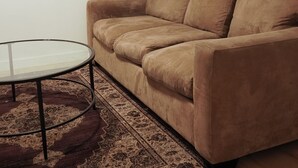 Ein Wohnzimmer mit einem braunen Sofa, einem runden Glastisch und einem gemusterten Teppich.