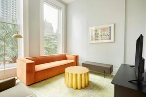 Uma sala de estar moderna com um sofá, uma mesa de centro redonda, um banco e uma televisão.