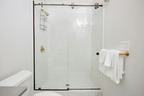 Casa de banho moderna com chuveiro em cabine de vidro, azulejos brancos tipo metrô e banheira branca.