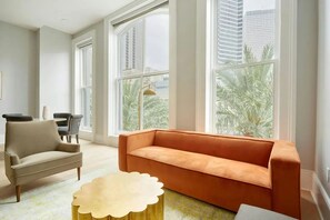 Ein modernes Wohnzimmer mit einem beigen Sofa, einem runden Couchtisch und Blick auf Palmen durch große Fenster.
