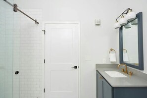 A modern bathroom with a white door, a glass shower enclosure, a sink with a gold faucet, and a mirror with a gold frame. - Sleeps 12 in the French Quarter • 100 Walk Score | The Harlequin by AvantStay (New Orleans)