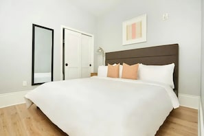 Quarto com cama grande, guarda-roupa, mesa de cabeceira e luminária.