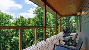 Terraza de madera con una silla colgante y una mesa, con vistas a un área boscosa.