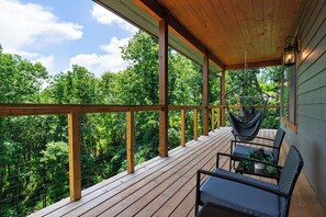 Eine Holzterrasse mit Hängesessel und Tisch, mit Blick auf ein bewaldetes Gebiet.