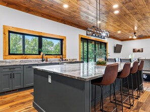 A modern kitchen with a large island, wooden ceiling, and large windows. - Sleeps 20 + Indoor Pool + Game Room Near Pigeon Forge | Spurling Retreat (Sevierville)