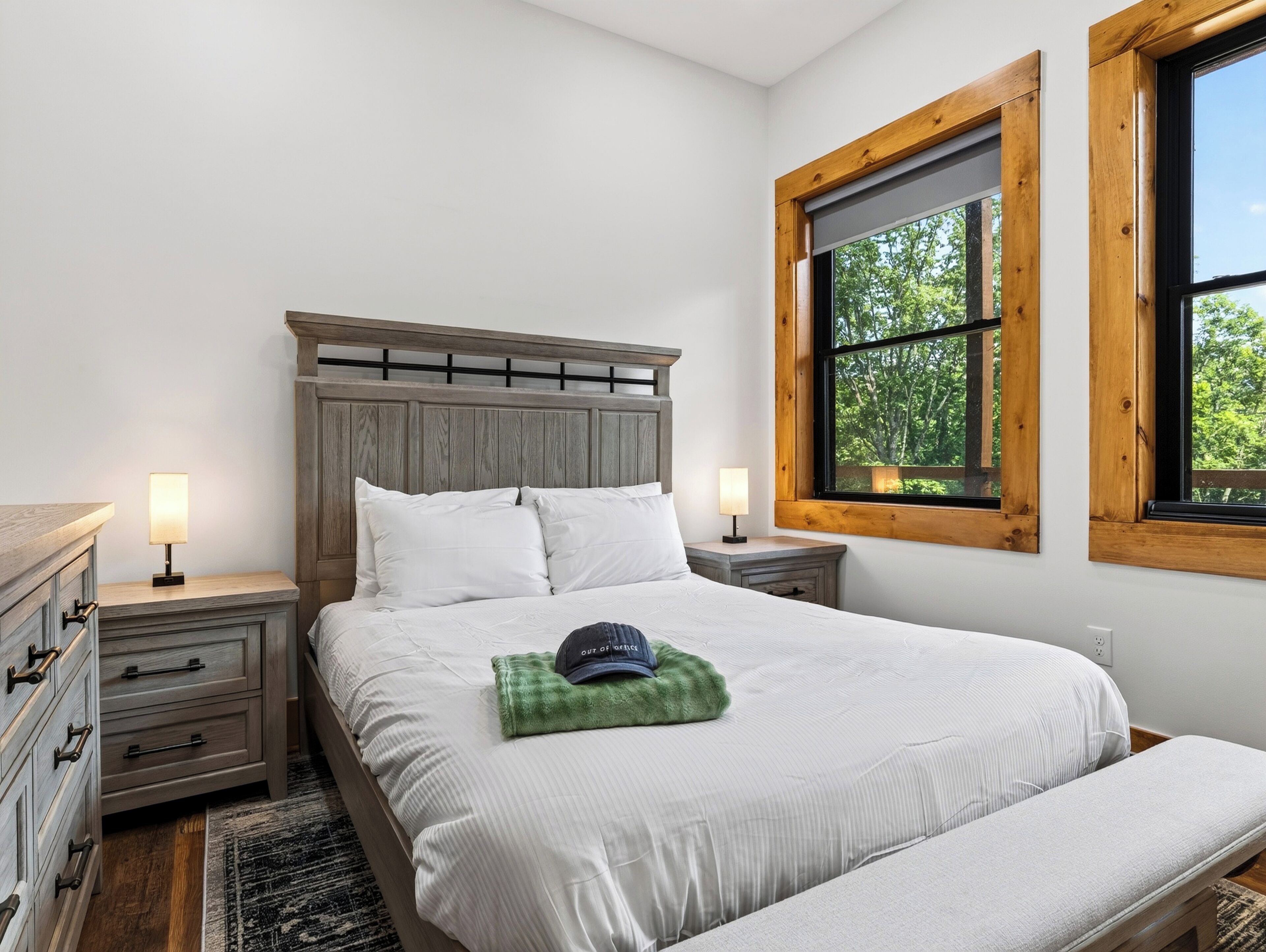 Un dormitorio con cama, mesitas de noche, cómoda y ventana con vistas a árboles.